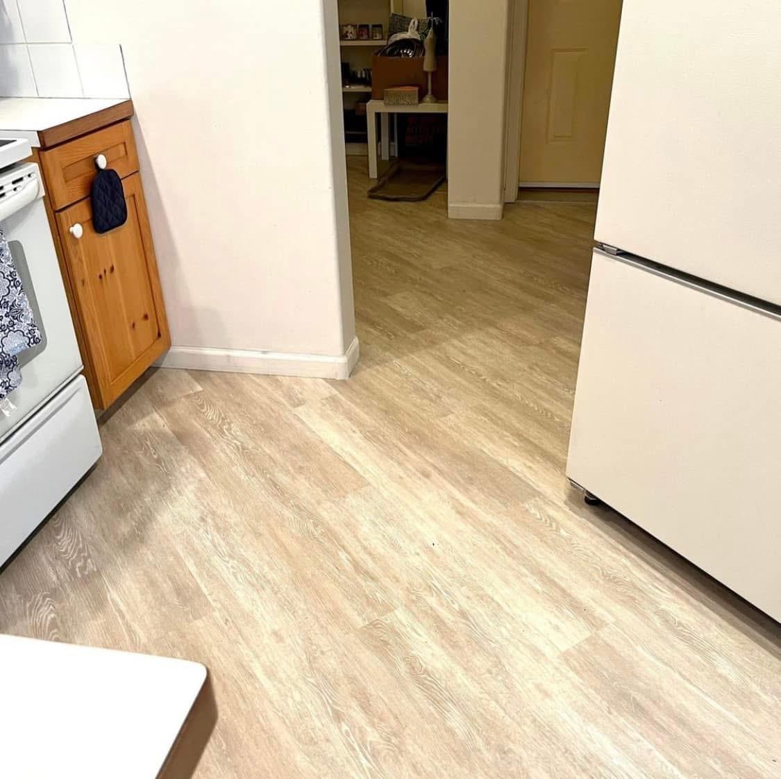 Kitchen with light wood-look plank flooring installed around the cabinets and appliances